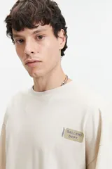 Remera de manga corta color beige, con corte holgado y hombros caídos. Presenta un estampado frontal con el texto "GALLERY DEPT." en un recuadro beige y el logo de la marca "mistral" en vertical.