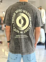 Remera oversize de color celeste con efecto gastado acid wash, mangas cortas y cuello redondo. Cuenta con un gran estampado circular en la espalda con la frase "Not all those who wander are lost" y texto adicional debajo.