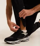 Pantalón deportivo de corte slim para hombre, confeccionado en poliéster color negro. Presenta cintura elástica con cordón de ajuste, bolsillos laterales y diseño ajustado en muslos y rodillas.