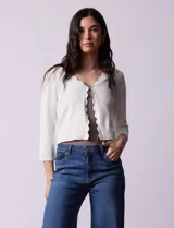 Cardigan tejido en hilado fino color blanco, marca Cable & Gauge. Abertura central con broche interno y terminación ondulada.