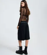 Bermuda tipo jorts de tiro bajo, confeccionada en denim de algodón. Presenta un corte recto y estructurado, con bolsillos funcionales, trabillas en la cintura y un cinturón decorativo de cadena metálica.