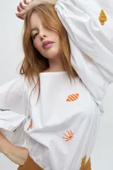Blusa blanca de algodón con mangas largas voluminosas y escote a la base. Presenta bordados artesanales coloridos con motivos marinos distribuidos en el frente y en las mangas.