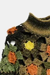 Jersey de punto con cuello subido y manga larga. Presenta un diseño de rayas horizontales en tonos verde y negro, con un panel superior decorado con calados y aplicaciones de flores tejidas en crochet de colores contrastantes.