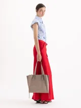 Bolso tipo tote de cuero color tostado con doble asa de hombro, detalles de hebillas metálicas en el frente y cierres laterales decorativos.