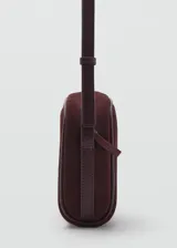 Bolso bandolera de tamaño pequeño confeccionado en piel de serraje color bordó, con cierre de cremallera y asa larga ajustable.