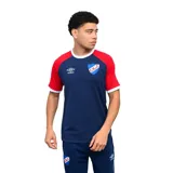 Remera deportiva Umbro del Club Nacional de Football, color azul con mangas en rojo y cuello redondo blanco. Presenta el logo de la marca y el escudo del club bordados en el pecho.