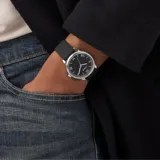 Reloj analógico Guess con caja de acero inoxidable plateado y esfera negra con números romanos. Cuenta con una malla de silicona negra y movimiento de cuarzo.