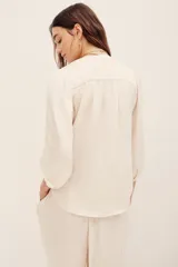 Camisa de poliéster color beige, con escote en V profundo, mangas 3/4 abullonadas y diseño fluido.