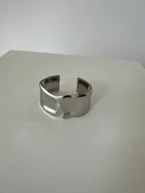 Brazalete rígido de diseño abierto con acabado pulido brillante y forma orgánica irregular.