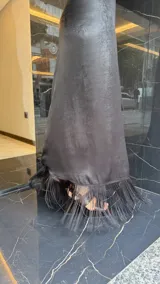 Vestido largo negro con escote halter cruzado y abertura frontal. El ruedo presenta un detalle de flecos.