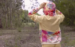 Canguro con capucha y cierre frontal, color beige con estampado de hojas en tonos marrones y amarillos. Mangas largas en color gris.