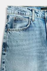Pantalón de jean tiro medio con diseño barrel, caracterizado por su pernera holgada que se estrecha hacia el tobillo. Presenta cinco bolsillos, cierre frontal con cremallera y botón, y detalle de raya planchada en el frente.