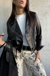 Chaqueta tipo biker de cuero vegano color negro, con solapas amplias, cierre frontal cruzado y detalles de cierres metálicos en los bolsillos y puños.