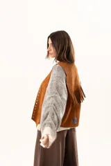 Chaleco oversize confeccionado en cuero descarne, con diseño de terminación en picos, detalle de tachas metálicas en los bordes frontales y flecos en la espalda.
