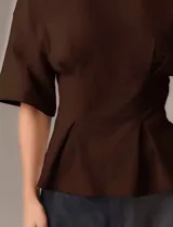 Remera marrón de diseño estructurado con silueta entallada, mangas amplias y detalles de pinzas frontales que aportan forma y volumen en la cintura.