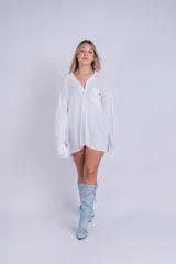 Camisa oversize de color blanco, con cuello clásico, cierre frontal de botones y un bolsillo en el pecho. Presenta mangas largas con puños anchos y un corte holgado.