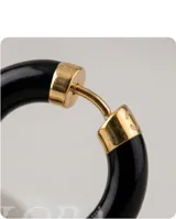 Aros tipo argolla de tamaño pequeño, con diseño minimalista en color negro brillante y detalle metálico en el cierre.