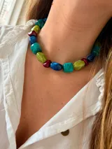 Collar tipo gargantilla compuesto por cuentas de resina de formas irregulares en tonos verde, azul y bordó, con cadena de acero quirúrgico para ajuste.