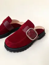 Zueco tipo mule de cuero color bordó, con puntera cuadrada y suela track negra. Presenta una tira ancha con hebilla metálica plateada sobre el empeine.