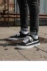 Championes urbanos de estilo skate, color negro con detalles en blanco. Presentan una franja lateral blanca distintiva, cordones blancos y suela de goma vulcanizada blanca.