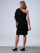 Vestido corto negro de RM Richards, con un hombro descubierto y una manga corta con volado. Presenta un aplique de lentejuelas plateadas en el tirante.