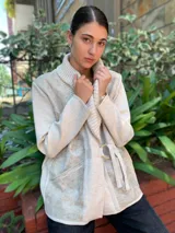 Chaqueta color crema con cuello tipo chal, cierre cruzado con cinturón y bolsillos laterales.