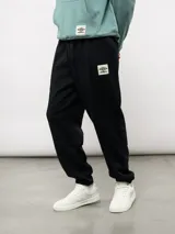 Pantalón jogger de felpa color negro, con cintura elástica, puños en los tobillos y etiqueta con el logo de la marca en la parte frontal.