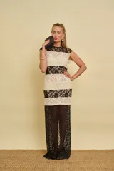 Vestido largo confeccionado en bandas combinadas de encaje negro y marfil, con diseño sin mangas, cuello redondo y transparencias en la parte inferior.