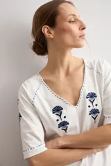 Remera blanca de manga corta con escote en V, decorada con delicados bordados florales en azul oscuro en el pecho, hombros y mangas.