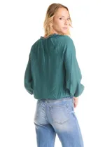 Blusa de satén color verde petróleo, con escote en V y cuello decorado con mostacillas bordadas. Presenta mangas largas con puños elásticos y ruedo también elastizado, brindando un ajuste cómodo y holgado.