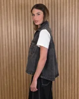 Chaleco de denim 100% algodón en color negro gastado, con cuello camisero, cierre frontal de botones metálicos y bolsillos delanteros con solapa.