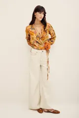 Camisa tipo cruzada (wrap) de manga larga con estampado floral multicolor en tonos mostaza y bordó. Cuenta con escote en V cruzado y detalle de lazo lateral con flor aplicada.