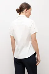 Camisa clásica blanca de manga corta, con cuello camisero y cierre frontal oculto con botones.