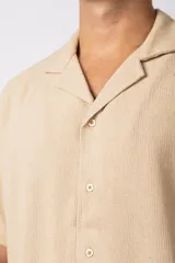 Camisa de manga corta con cuello cubano, confeccionada en lino entramado de textura natural. Presenta un corte relajado y cierre frontal con botones.
