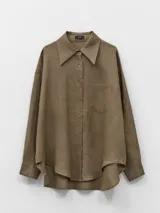 Camisa oversize de lino color marrón, con cuello amplio, cierre frontal abotonado y bolsillo de parche en el pecho. Presenta un ruedo asimétrico más largo en la espalda.