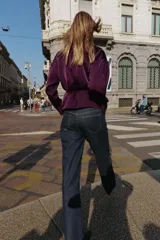 Camisa satinada de color violeta oscuro, con cuello solapa, escote en pico y manga larga. Presenta un detalle de cinturón fino ajustable a tono en la cintura y cierre frontal con botones.