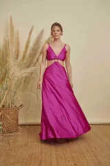 Vestido largo de satén color fucsia, con escote en V, aberturas laterales en la cintura y detalle de aro metálico en el centro del pecho. Posee breteles finos y falda con caída fluida.