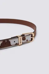 Cinturón de eco-piel con estampado de vaca en tonos blanco y marrón, con hebilla dorada.