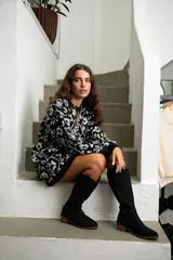 Bota de caña alta estilo western, confeccionada en gamuza negra con detalles bordados sutiles en la caña y el empeine. Cuenta con un taco bajo y suela de madera.