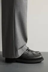 Zapato de vestir tipo brogue negro, con detalles de perforaciones decorativas y suela track dentada.