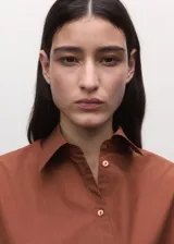 Camisa de algodón color marrón, de diseño cruzado estilo sobre con lazo lateral para anudar, cuello camisero, manga larga y calce amplio.
