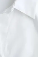 Camisa blanca de corte entallado con cuello clásico, cierre frontal de botones, mangas largas con puños abotonados y pinzas frontales y traseras para un ajuste estilizado.