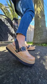 Zueco cerrado 100% de cuero color tostado con efecto desgastado, detalles en cuero negro y una tira con hebilla metálica decorativa.