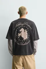 Sudadera de manga corta con corte relajado, confeccionada en algodón con interior de rizo. Presenta cuello redondo con detalle de costura en V, efecto lavado y estampado gráfico en el frente.