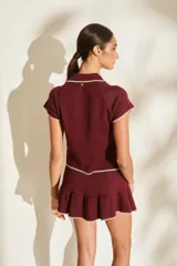 Falda corta de tejido de punto color marrón, con detalles de costuras a contratono en blanco y diseño con volados fruncidos en el ruedo.