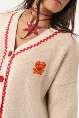 Saco oversize tejido con ilustraciones inspiradas en corales, peces, estrellas de mar y tortugas. Presenta galón picot en rojo en cartera y puños, y botones a tono.