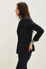 Saco de corte sastrero en color azul marino, con solapas clásicas, cierre frontal de un botón y bolsillos laterales con solapa. Presenta una estructura entallada con hombreras.