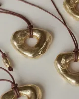 Collar con dije de forma irregular en tonos dorados y plateados, suspendido de un cordón doble de algodón negro.