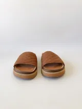 Sandalias chatas color camel, con diseño capitoneado en la tira superior. Fabricadas en cuero.