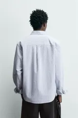 Camisa de corte regular fit confeccionada en tejido de algodón con diseño de rayas verticales. Presenta cuello abotonado, manga larga con puños abotonados, bolsillo plastrón en el pecho y cierre frontal con botones.